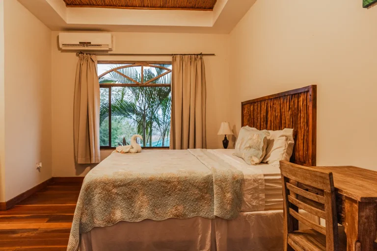 Interior of a Studio with kitchen at La Jolla de Guasacate, Nicaragua, showing two beds, a high vaulted ceiling, and an arched glass door leading to a private balcony with garden views.